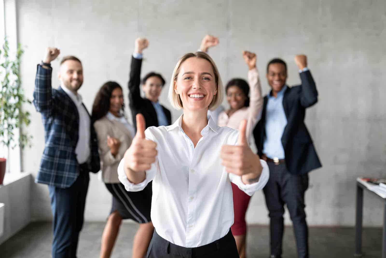 Successful Business Team. Businesswoman Gesturing Thumbs Up Standing With Joyful Employees In Modern Office. Great Deal, Leadership And Teamwork Concept. Selective Focus